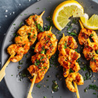 Tasty appetizing prawns on skewers with lemon and spices served on plate. View from above with copy space.